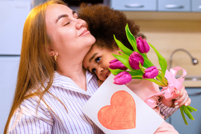 mom hugs child with card and flowers