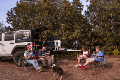 friends sitting on chairs at campsite with Jeep