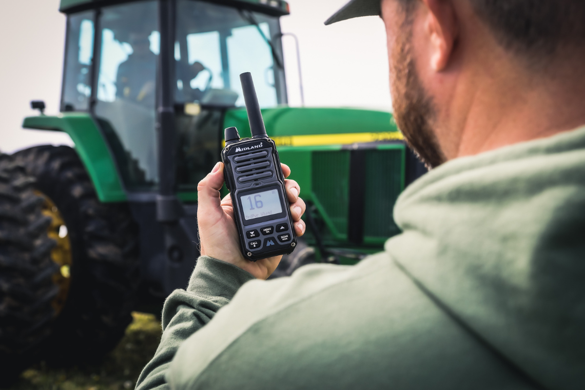 man holds walkie talkie in front of tractor