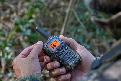 man holds camo walkie talkie in woods