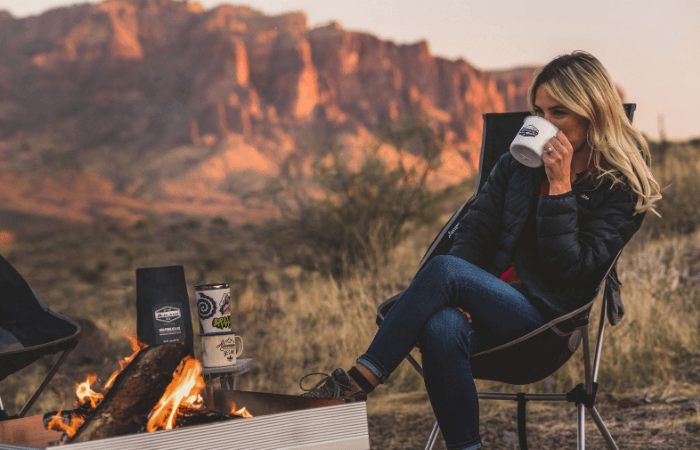 woman drinks coffee by campfire