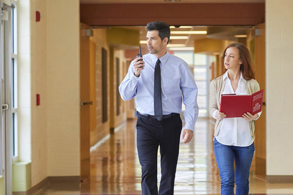 man and woman walk through school hallway with business radio
