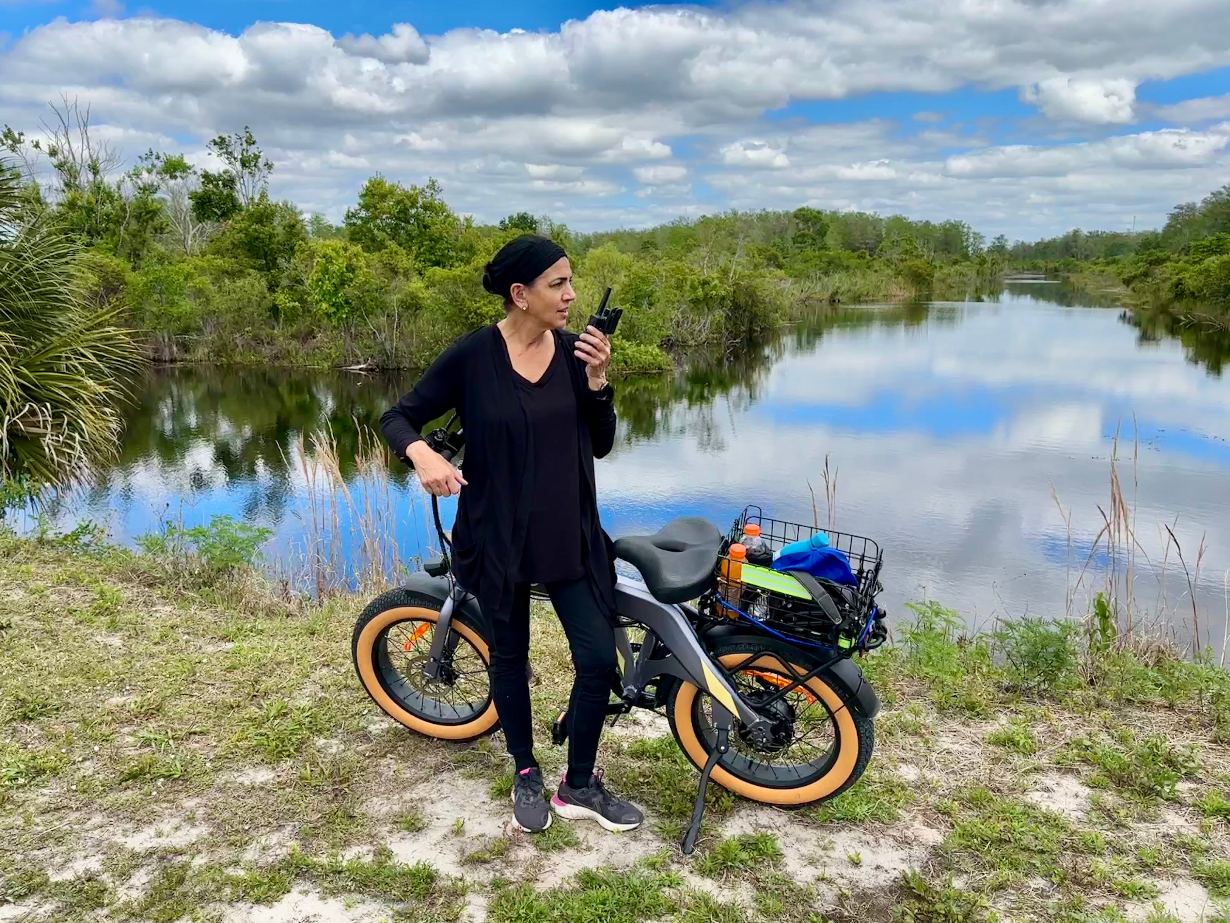 woman stands by bike and lake with walkie talkie
