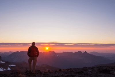 man overlooks summit of mountains at sunrise