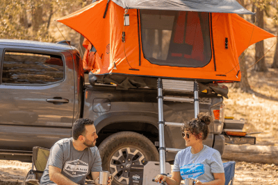 man in woman sit in chairs under rooftop tent