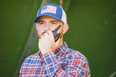 man with plaid shirt and hat talking on radio in front of tractr