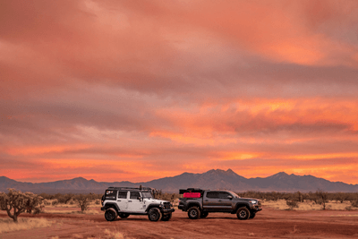 two overlanding vehicles on trail with mountains and sunset in background