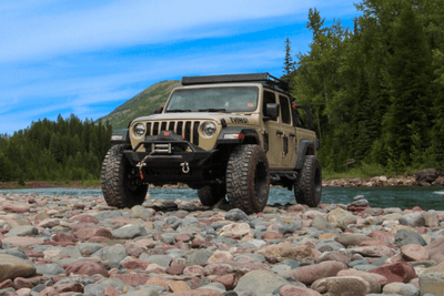 Jeep on rocks near water with trees in background