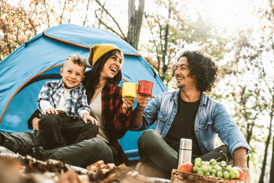 man and woman hold coffee mugs at campsite with toddler
