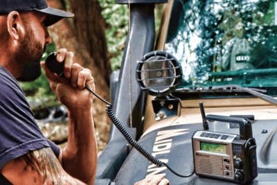man uses basecamp radio on the hood of his vehicle in the forest