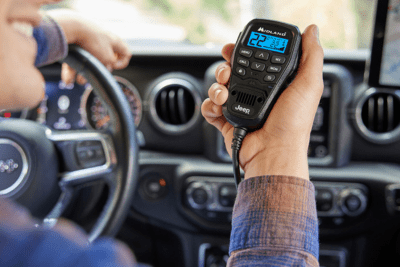 man's hand holds Midland Jeep-branded radio microphone in his Jeep