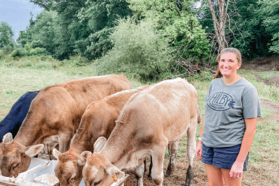 woman stands by cows eating