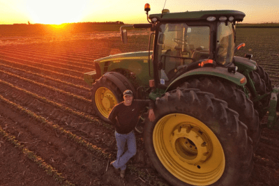 farmer stands by tractor in field with sunset