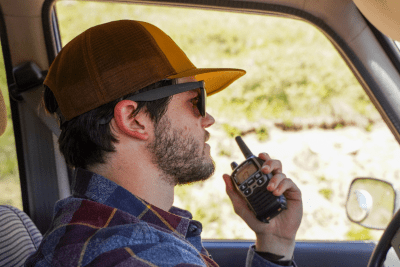 man wearing hat in vehicle uses silver and black walkie talkie