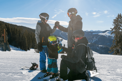 family holds hands and walkie talkies on top of snowy mountain on ski trip
