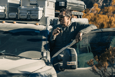 man stands on ledge of his overlanding vehicle holding radio mic