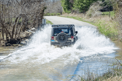 Jeep goes through water crossing next to treets