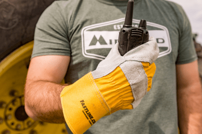 farmer wearing glove holds a walkie talkie in front of tractor