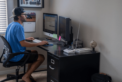man works from desk at home with NOAA Weather Radio on his desk