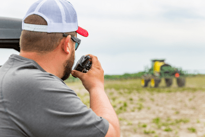 farmer looks at tractor in field while talking on a walkie talkie