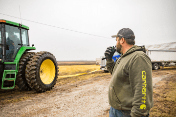 famer holds walkie talkie by tractor