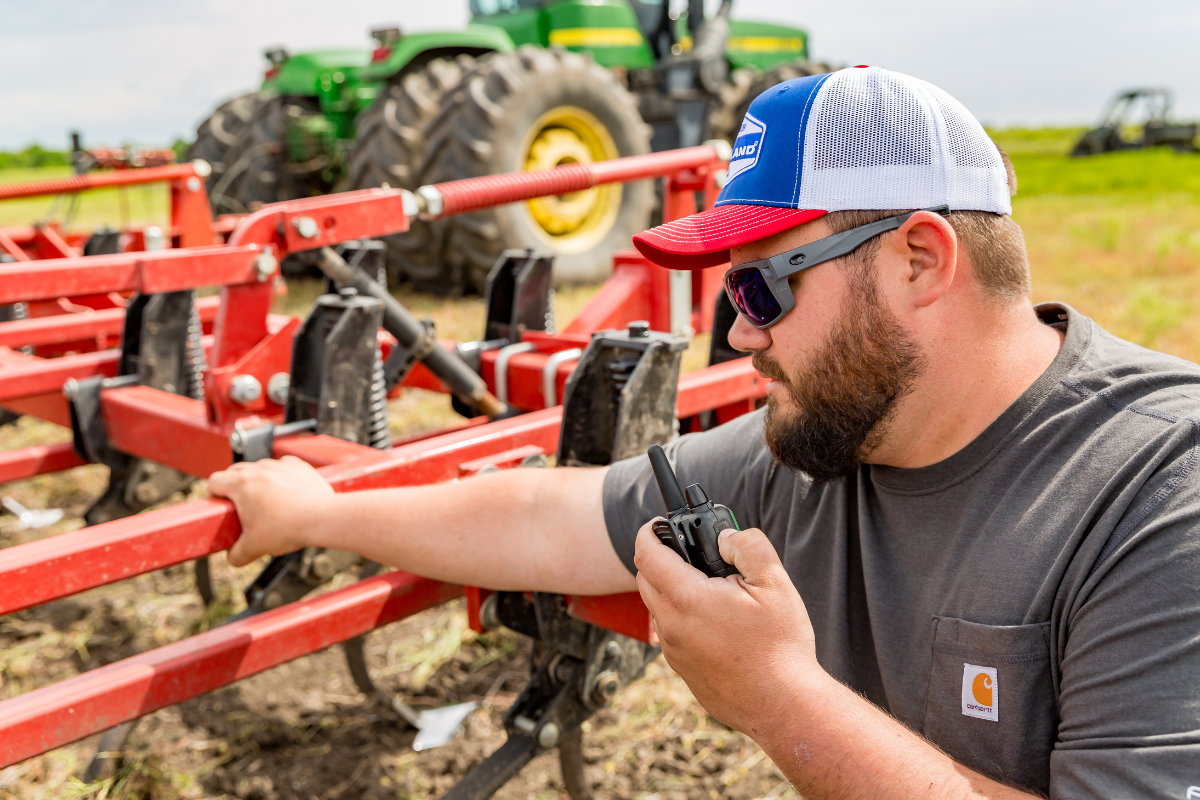 man holds walkie talkie by farm equipment