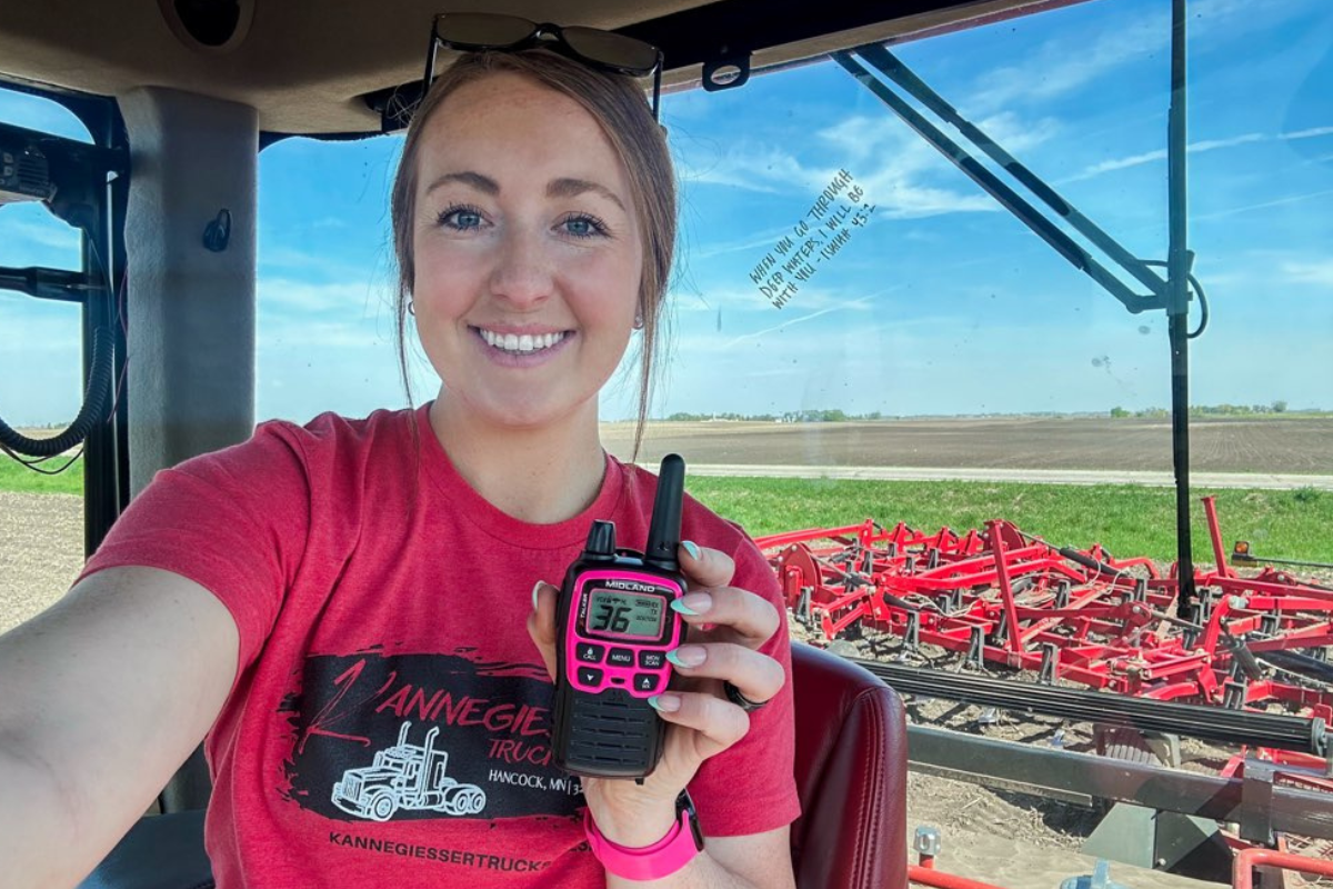 female farmer holds pink walkie talkie in tractor cab