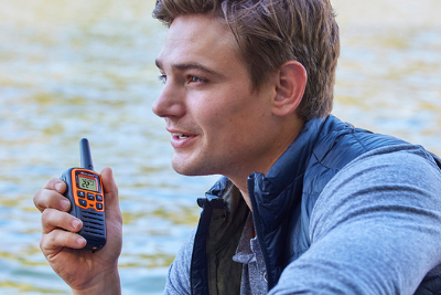 man holds orange walkie talkie by water