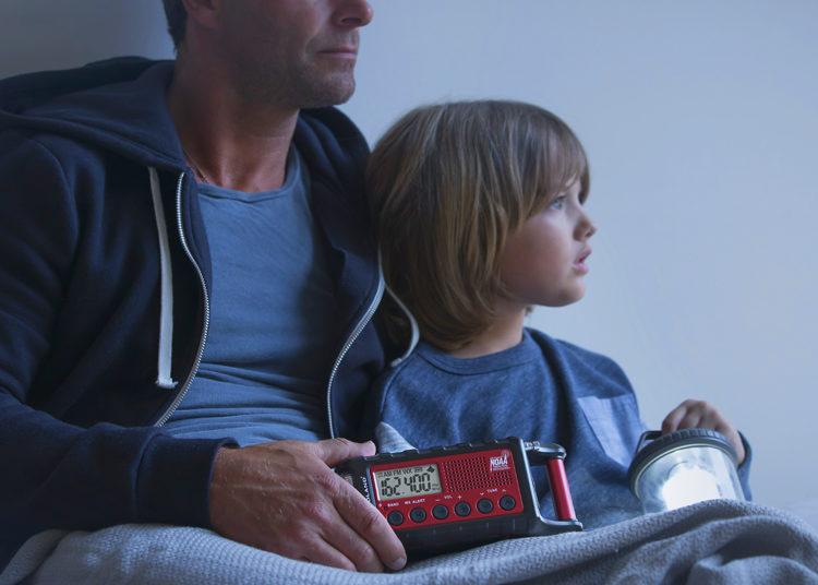 father and son hold lantern and emergency radio during storm
