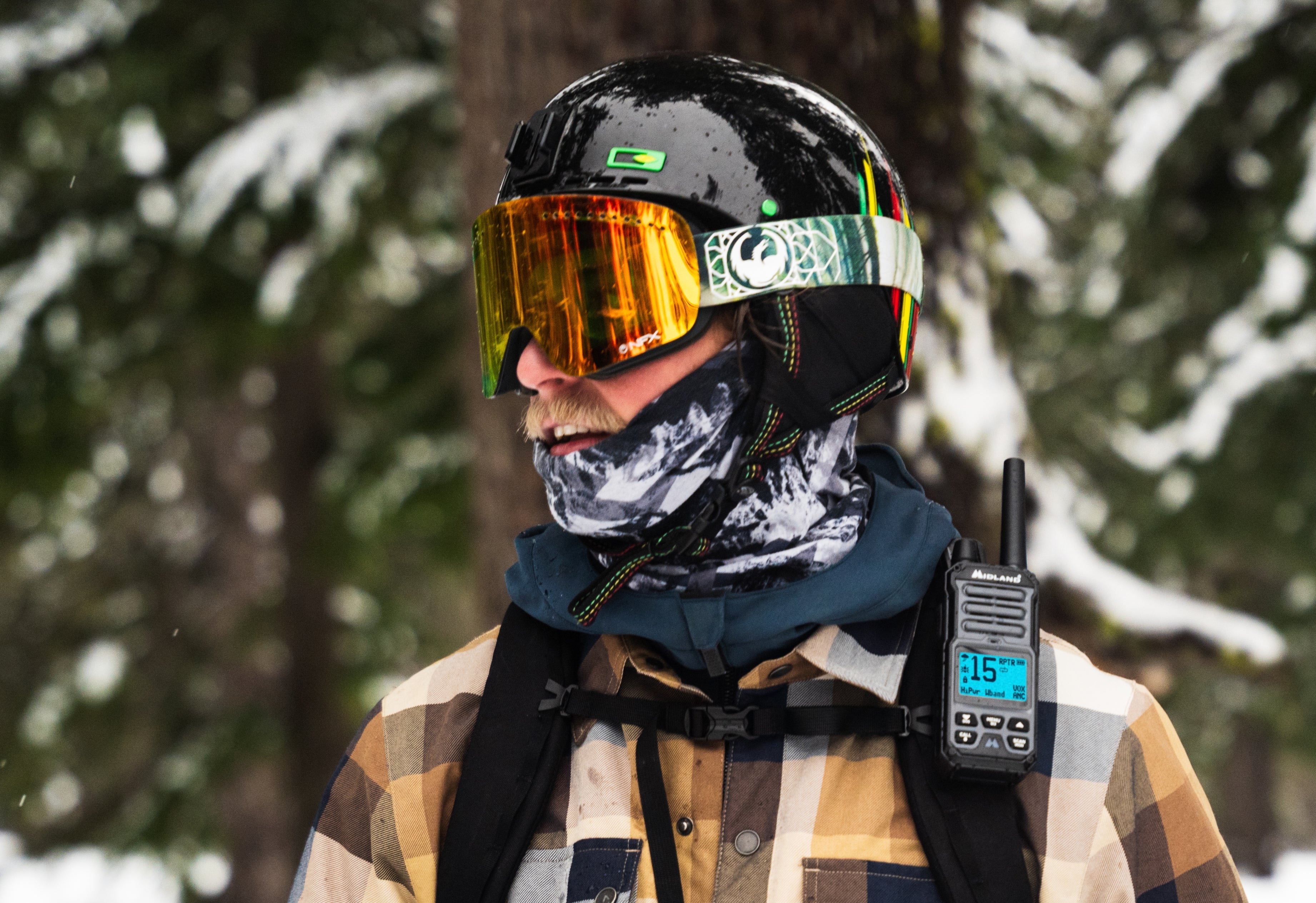 Man in winter gear with a helmet and goggles standing in a snowy forest.